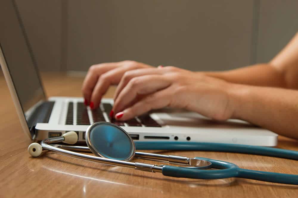 Person typing on laptop next to stethoscope